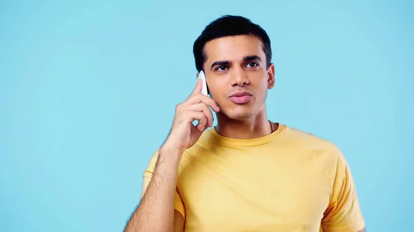 Young man in yellow t-shirt talking on cellphone isolated on blue — Stock Photo