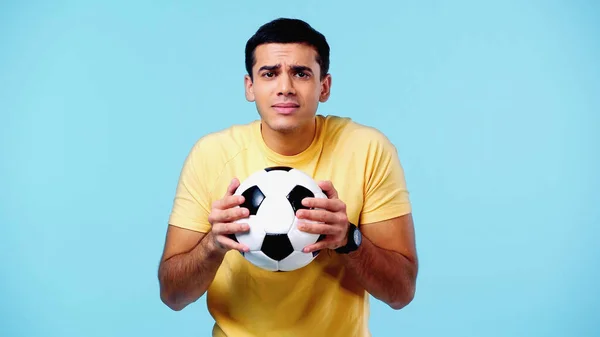 Scared young man in yellow t-shirt holding football isolated on blue — Stockfoto