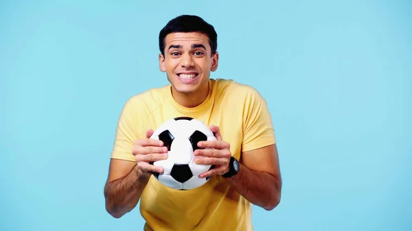 Jovem feliz em camiseta amarela segurando futebol isolado em azul — Fotografia de Stock