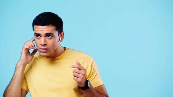 Young man adjusting wireless earphones isolated on blue — Fotografia de Stock