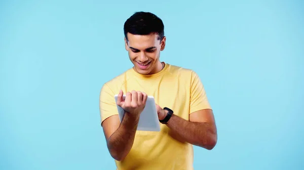 Heureux jeune homme en t-shirt jaune en utilisant tablette numérique isolé sur bleu — Photo de stock