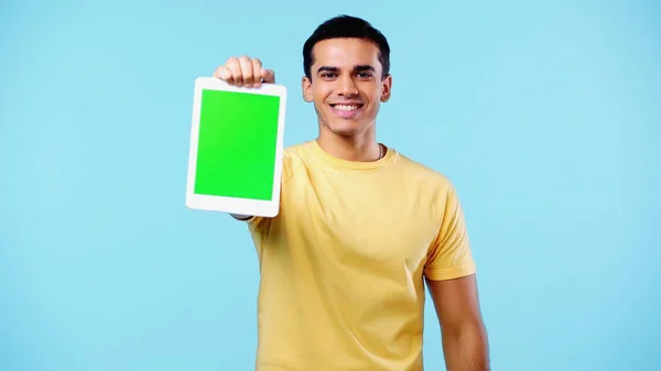 Heureux jeune homme en t-shirt jaune tenant tablette numérique avec écran vert isolé sur bleu — Photo de stock