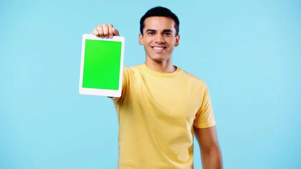 Задоволений молодий чоловік у жовтій футболці тримає цифровий планшет із зеленим екраном ізольовано на синьому — стокове фото