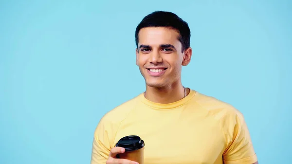 Cheerful young man in yellow t-shirt holding paper cup isolated on blue — Stock Photo