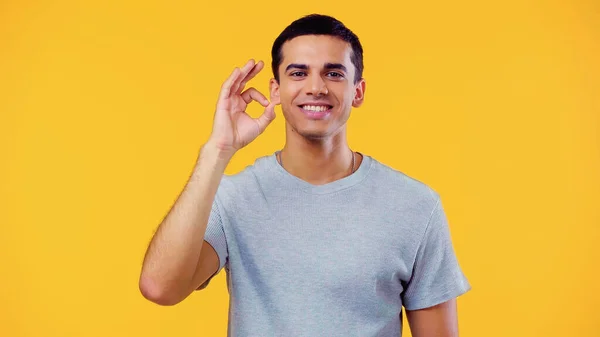 Cheerful young man in t-shirt showing ok sign isolated on yellow — Stock Photo
