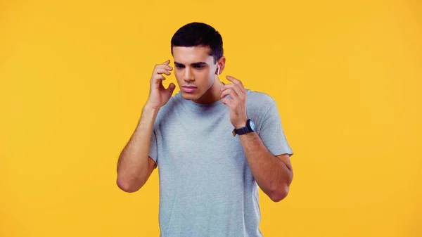 Confuso joven en camiseta ajustando auriculares inalámbricos aislados en amarillo - foto de stock