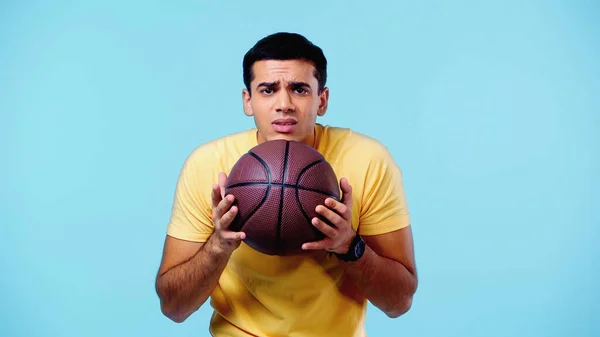 Verängstigter Mann in gelbem T-Shirt hält Basketball isoliert auf blau — Stockfoto