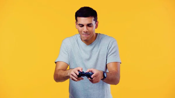 KYIV, UKRAINE - DECEMBER 22, 2021: cheerful young man looking at joystick and biting lips isolated on yellow — Foto stock