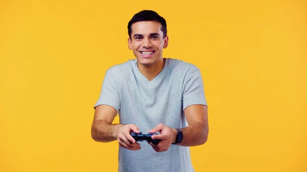 KYIV, UKRAINE - DECEMBER 22, 2021: joyful young man holding joystick and playing video game isolated on yellow — Stock Photo