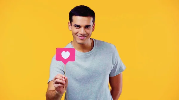 Happy young man in t-shirt holding heart on stick isolated on yellow — Stock Photo