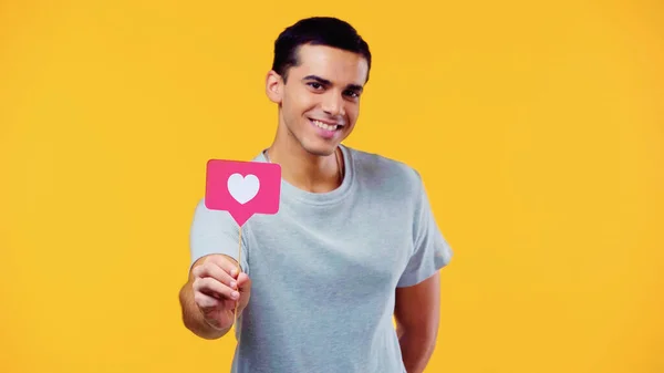 Fröhlicher junger Mann im T-Shirt mit Herz am Stock, isoliert auf gelb — Stockfoto