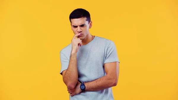 Pensive young man in t-shirt touching lips isolated on yellow — Foto stock