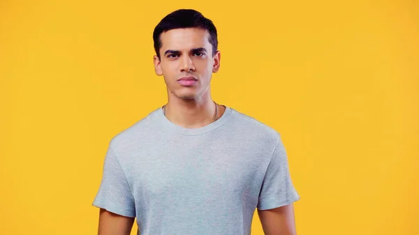 Serious young man in t-shirt looking at camera isolated on yellow — Stockfoto