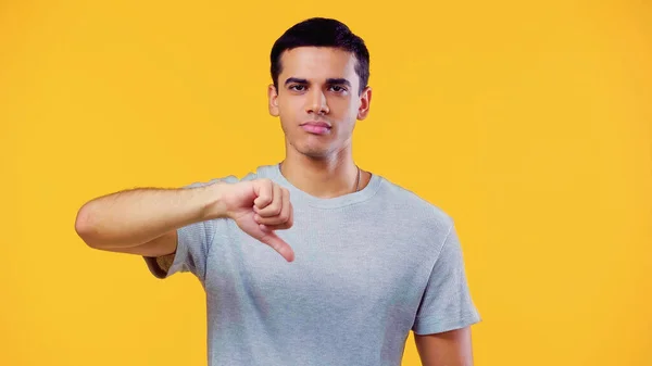 Young man in t-shirt showing dislike isolated on yellow — Stock Photo
