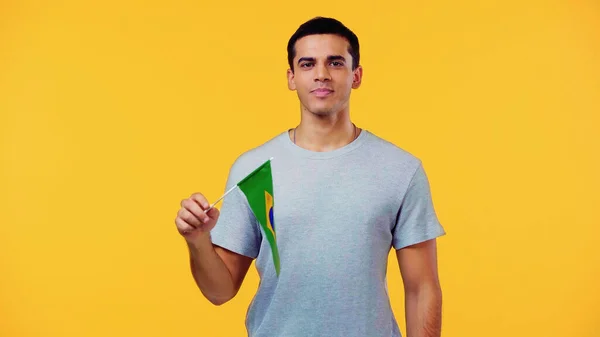 Young man in t-shirt holding small flag of brazil isolated on yellow — Stock Photo