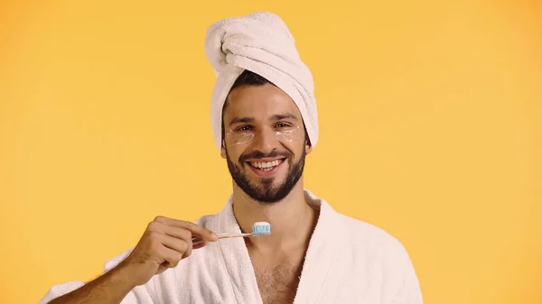 Homme souriant avec des patchs pour les yeux tenant la brosse à dents isolée sur jaune — Photo de stock