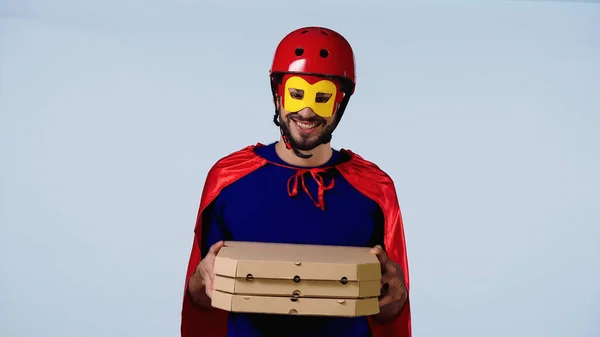 Hombre sonriente en traje de superhéroe cajas de espera con pizza aislada en azul — Stock Photo