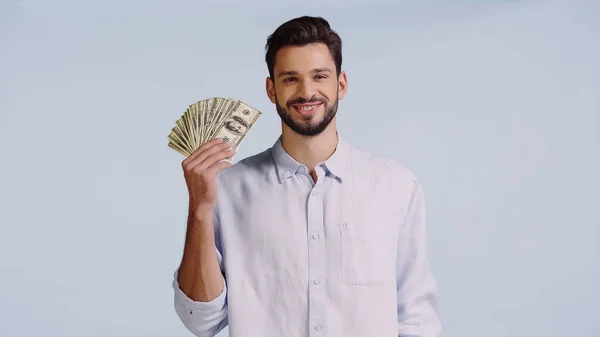 Happy man in shirt looking at camera while showing dollars isolated on blue — Stock Photo