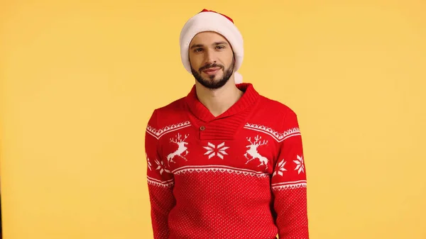 Uomo sorridente in cappello di Babbo Natale e maglione rosso isolato su giallo — Foto stock