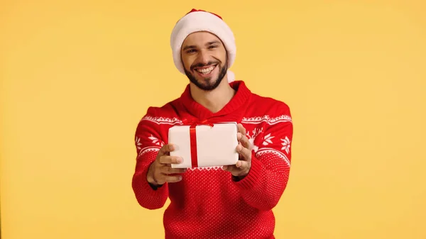 Felice uomo in cappello di Babbo Natale contenente scatola regalo isolato su giallo — Foto stock
