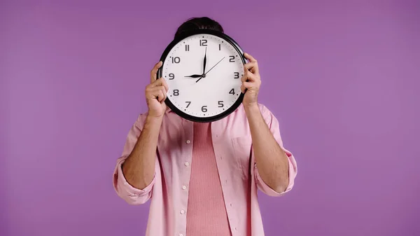 Young man obscuring face with clock isolated on purple — Foto stock