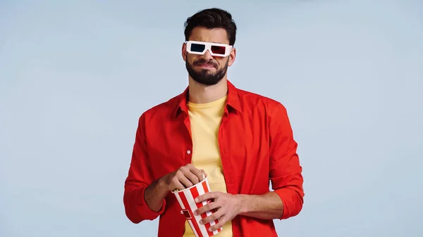 Unzufriedener Mann in 3D-Brille schaut Film und hält Popcorn-Eimer isoliert auf blauem Grund — Stockfoto
