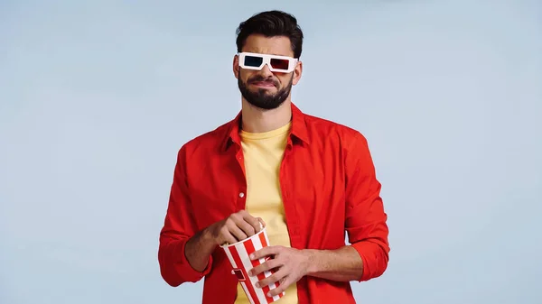 Hombre insatisfecho en gafas 3d viendo película y sosteniendo palomitas de maíz cubo aislado en azul — Stock Photo