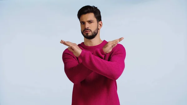 Serious man in pink sweater crossing hands isolated on blue — Stockfoto