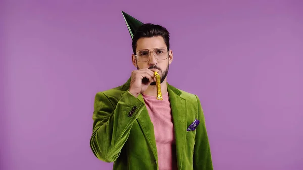 Man in green jacket blowing in party horn isolated on purple — Foto stock