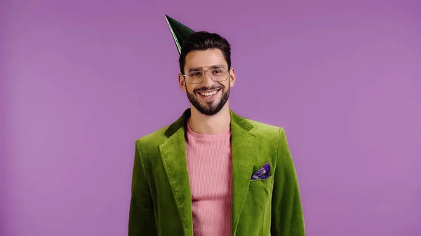 Hombre alegre en chaqueta verde y gorra de fiesta sonriendo aislado en púrpura - foto de stock