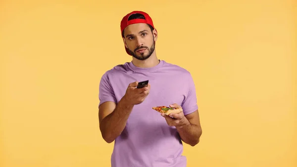 Barbudo hombre con pizza viendo tv aislado en amarillo - foto de stock