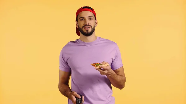 Щасливий чоловік з піцою дивиться телевізор ізольовано на жовтому — стокове фото