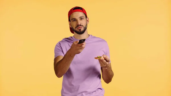 Homem barbudo segurando pizza e canais de comutação isolados no amarelo — Fotografia de Stock