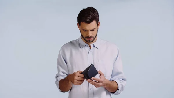 Uomo triste guardando portafoglio vuoto isolato su blu — Foto stock