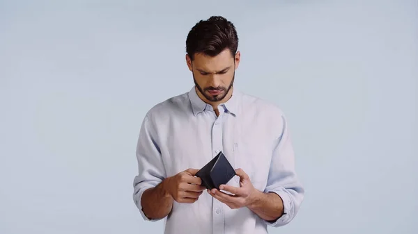 Hombre triste mirando la cartera vacía aislado en azul - foto de stock