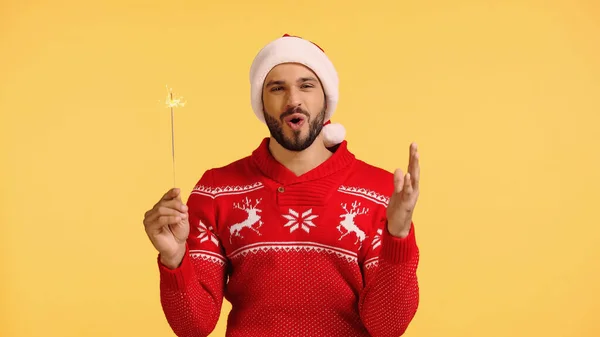 Excited man holding shiny sparkler isolated on yellow — стоковое фото