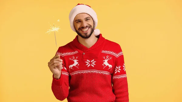 Cheerful man holding shiny sparkler isolated on yellow — Stockfoto