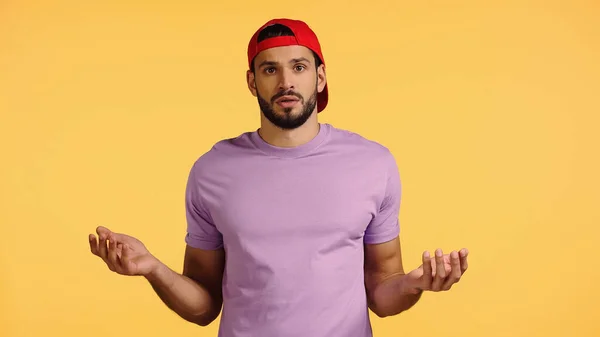 Confused and bearded man in cap showing shrug gesture isolated on yellow — Stock Photo