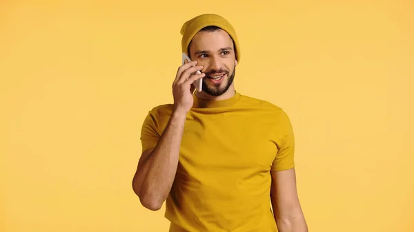 Positive man in beanie hat talking on smartphone isolated on yellow — Stock Photo