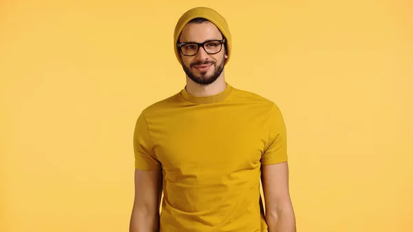Happy young man in beanie hat, glasses and t-shirt isolated on yellow — Stock Photo