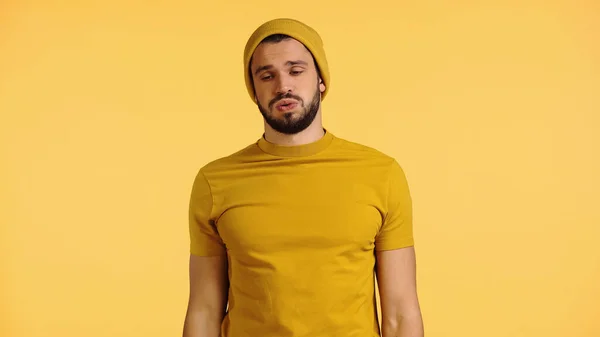 Tired young man in beanie hat and t-shirt puffing cheeks isolated on yellow — Fotografia de Stock