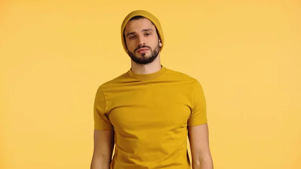 Jovem triste em chapéu gorro e t-shirt isolado em amarelo — Fotografia de Stock