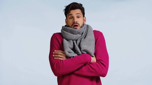 Sick man in pink sweater and scarf standing with crossed arms and sneezing isolated on blue — Stock Photo