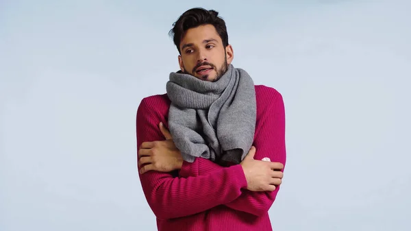 Hombre enfermo en suéter rosa y bufanda de pie con los brazos cruzados mientras se siente frío aislado en azul - foto de stock