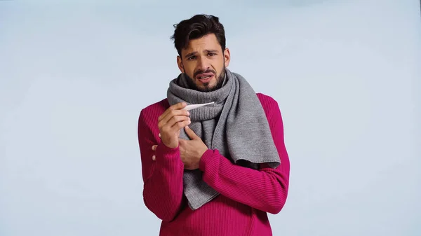 Uomo malato in maglione e sciarpa con termometro digitale isolato su blu — Foto stock