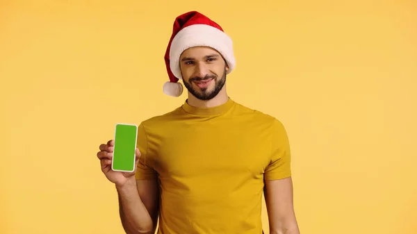 Happy man in santa hat holding smartphone isolated on yellow — стоковое фото