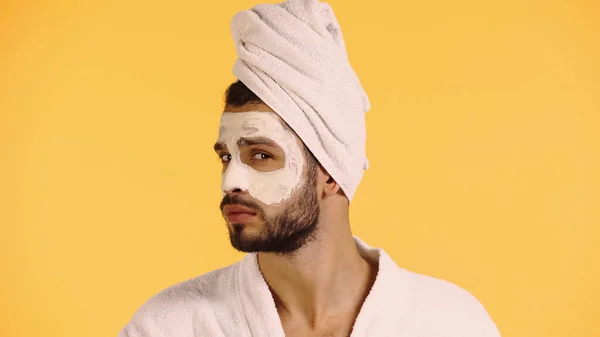 Homme barbu avec masque d'argile sur le visage en regardant la caméra isolée sur jaune — Photo de stock