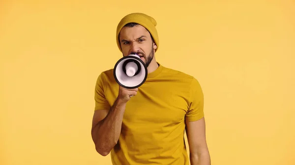 Displeased man in beanie hat talking in loudspeaker isolated on yellow — Stock Photo