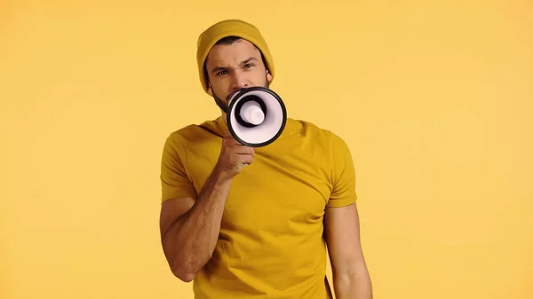 Man in beanie hat talking in loudspeaker isolated on yellow — Stock Photo