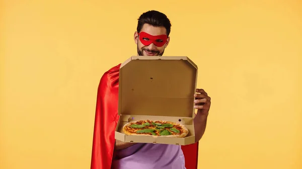 Happy man in superhero costume opening box with pizza isolated on yellow — Stock Photo